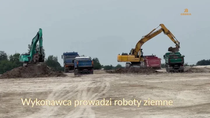 Na placu budowy dwa koparki ładują ziemię do ciężarówek podczas robót ziemnych.