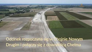 Widok z lotu ptaka na budowę drogi przez pola uprawne, z nanieszonym logotypem GDDKIA.